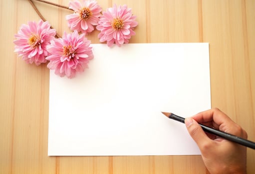 A woman's hand holding a pencil and a piece of paper with pink flowers on a wooden table photo