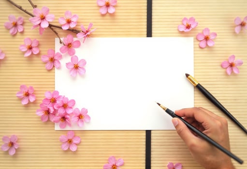Woman's hand holding a pen and paper with pink cherry blossom on wooden table photo