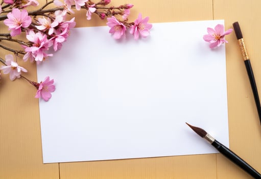 A blank sheet of paper, a paint brush and a cherry blossom branch on a wooden table photo