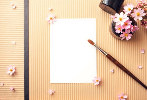 A blank paper, a paint brush and a cherry blossom on a brown paper background photo