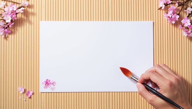 A person's hand holding a brush and a piece of paper with cherry blossoms photo
