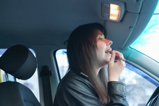 Young woman applies lipstick while sitting in car during daytime commute photo