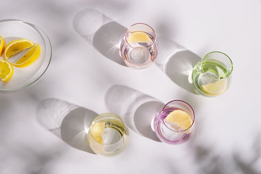 Drinking natural water in colored glass glasses with slice of lemon on white background in sunny day photo