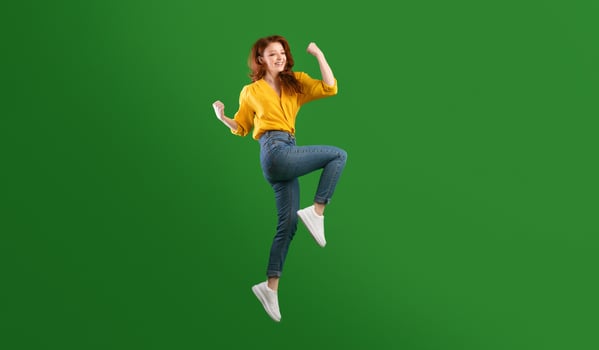 Winner. Happy Millennial Girl Jumping Shaking Fists In Joy Celebrating Victory Over Green Background. Studio Shot, Empty Space photo