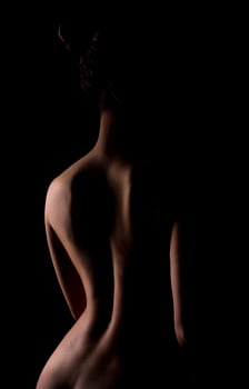 Graceful line of back of young naked woman on black background, photo art