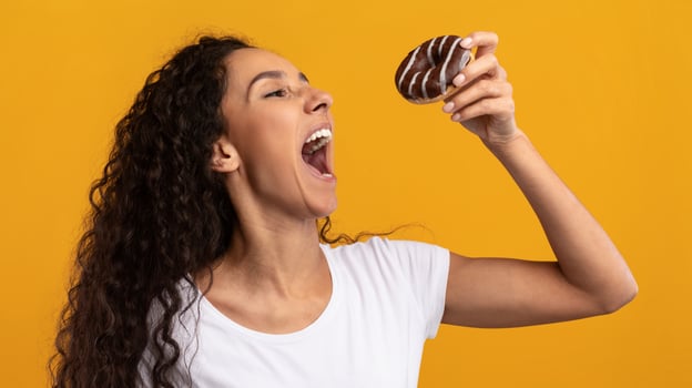 Cheat Meal. Funny Hungry Latin Lady Holding Doughnut Eating Junk Food Posing With Wide Open Mouth Over Yellow Orange Studio Background. Unhealthy Nutrition And Binge Eating Habit Concept photo