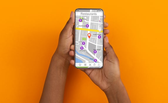 African American girl holding cellphone with map and restaurant navigation pointers on screen, orange background. Collage. Panorama photo