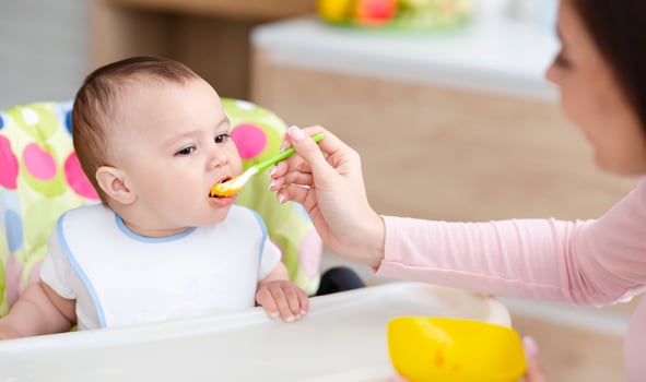 Mother feeding her cute toddler on high chair at kitchen, free space photo