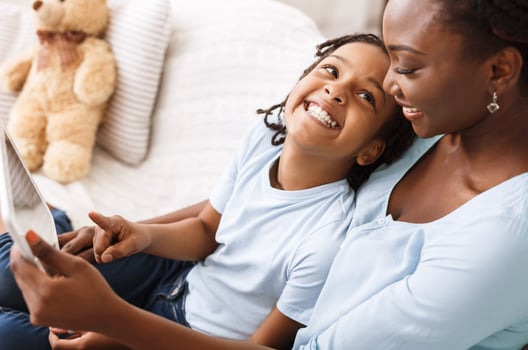 Togetherness Concept. African american mom and daughter sitting on couch together using digital tablet. Free Space photo