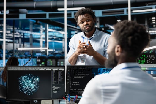 Server farm manager supervising engineer looking at data analysis graph to reduce failures. Data center team leader overseeing worker looking at AI visualization dashboard to pinpoint gear glitches photo