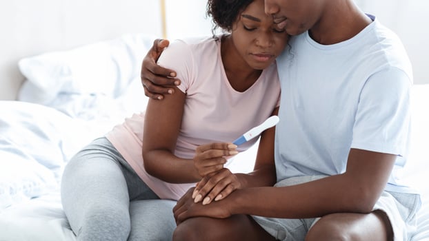 Upset black couple holding negative pregnancy test, husband hugging his depressed wife, bedroom interior, empty space. Sad african american family looking at pregnancy test, copy space photo