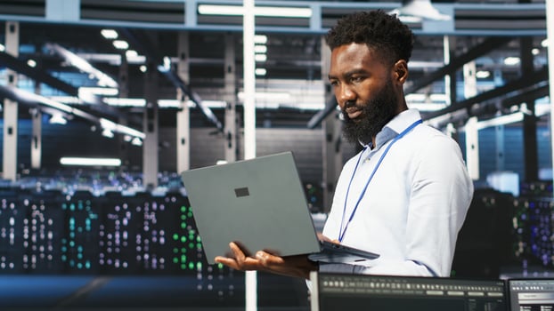 Data center programmer uses node tree software to identify equipment performance issues. African american server farm worker reviews data analysis graph to minimize hardware failures, camera B photo