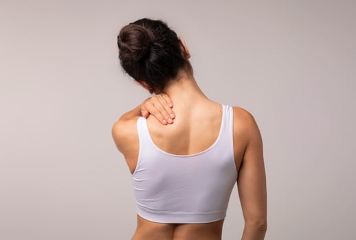 Unrecognizable brunette woman with neck and back pain rubbing her painful body neck area, lady suffering from office syndrome, back view, grey studio background, copy space photo