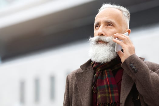 Elderly businessman walking by city, having phone call, looking at copy space, panorama, business center background. Senior grey-haired man coming back from job, talking on mobile phone photo