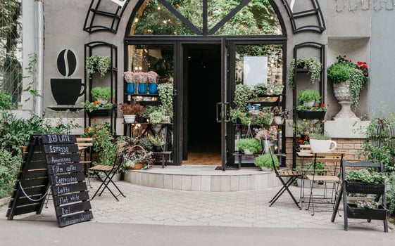 Eco cafe on street and flower studio, small business in city, reopening after covid-19, outdoor interior. Sign board with menu, tables for clients, potted plants on shelf at modern store, nobody photo