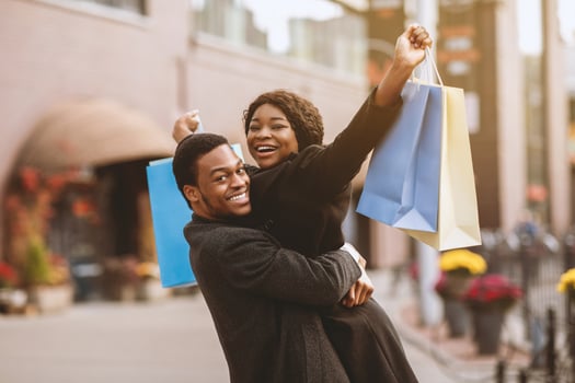 Good bought at low price during seasonal sale and Black Friday. Happy millennial man in coat picks up wife with colored bags and rejoice successful purchase, near modern city mall, free space photo