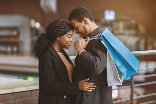 Romance for two, tenderness and date during seasonal sales and Black Friday. Young african american couple in love with colored shopping bags hugging at city mall ready to buy, side view, free space photo