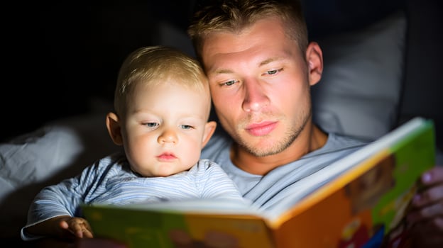 Father and Toddler Son Reading Book Together in Bed at Night photo
