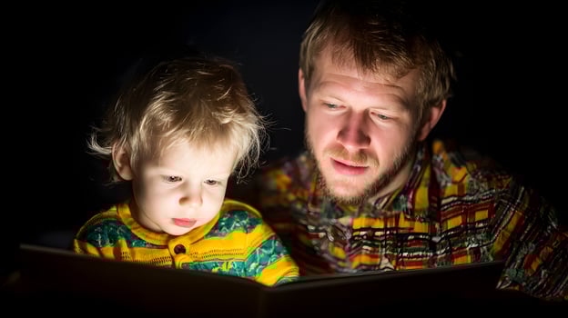 Father and Toddler Son Reading Book Together at Night Low Light photo