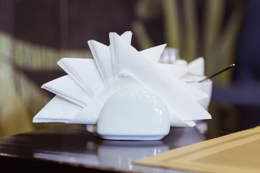 White napkins in holder on wooden table, close up photo