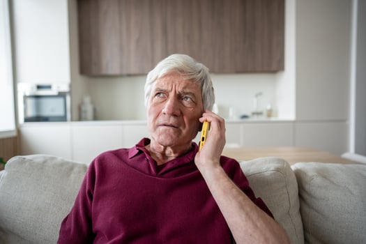 Suspicious anxious elderly man with phone at home, targeted by scam artists, telemarketing fake news photo