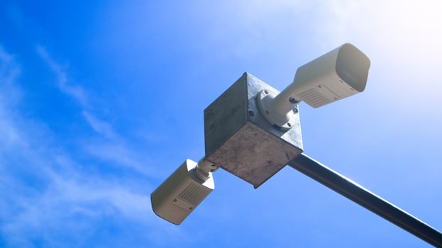Two CCTV cameras on a metal box for outdoor installation. The cameras are separated on opposite sides. The metal legs extend out. Under the bright blue sky. photo