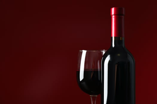 Bottle and glass with wine against red background, copy space photo
