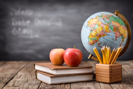 School supplies on wooden desk in front of chalkboard with math lesson written on it photo
