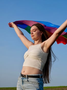 A woman in a white tank top holding a rainbow flag photo