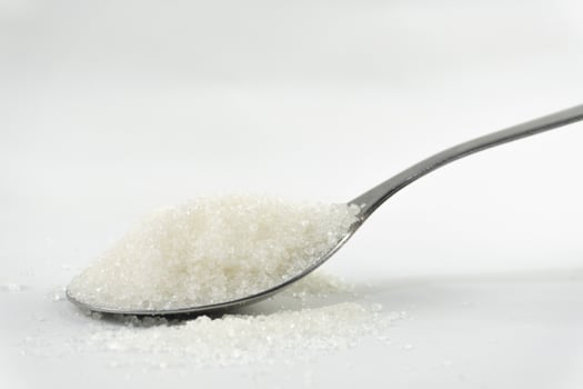 A silver spoon holds a mound of granulated sugar, set against a stark white background, emphasizing its sweetness and dietary implications. photo