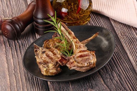 Grilled lamb chops on a black plate with rosemary sprigs photo