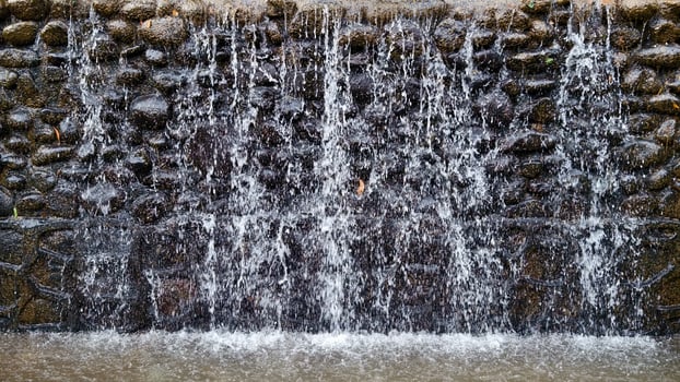 Artificial Waterfall with Cascading Water Over a Textured Rock Wall Feature in a Park photo