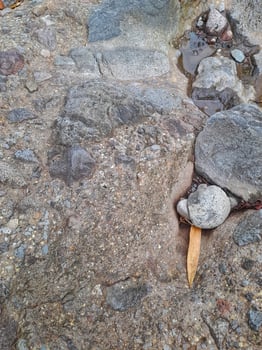 Close up of a natural rock surface with a rough, uneven texture, visible cracks, and earthy tones, showing signs of weathering and mineral deposits. photo