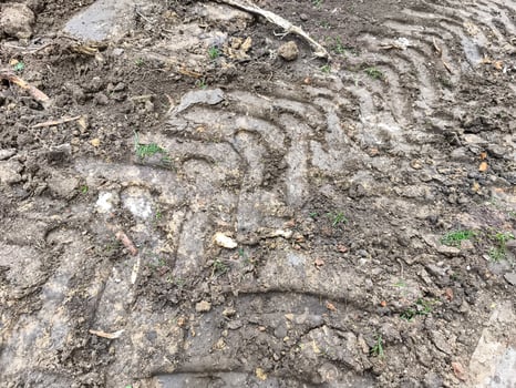 The dirt is muddy and has tire tracks in it. The tire tracks are in a zigzag pattern photo