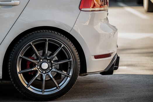Rear view of a white car highlighting the back wheel and brake system. The car features a shiny, sporty alloy wheel with a red brake photo