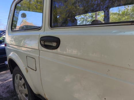 A white car with a black handle on the door. The car is parked in front of a building photo