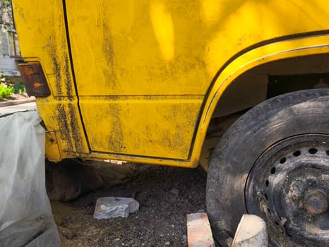 A yellow truck with a dirty back and a black tire. The truck is parked on a dirt road, with a pile of bricks nearby photo