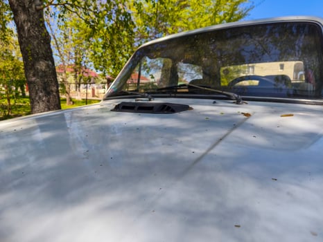 A white car with a black hood and a black grill. The hood is open and there is a lot of dirt on it. The car is parked in a parking lot photo