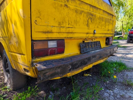 A yellow old truck with a black tail light. The back of the truck is rusted and dirty photo