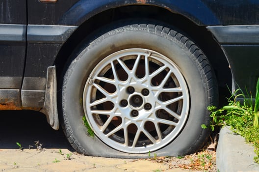 A black car with a flat tire. The tire is missing a piece and is sitting on the ground photo