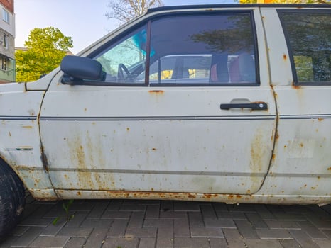 A rusted old car with a dirty windshield and a dirty door. The car is parked on a brick road photo