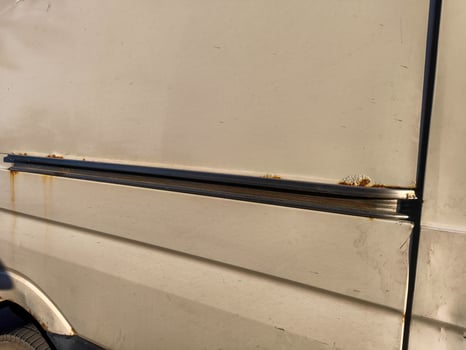 A rusted van door with a metal strip on the side. The door is open and the strip is bent photo