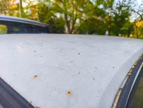 A car with a dirty windshield and a rusty bumper. The car is parked in a parking lot photo