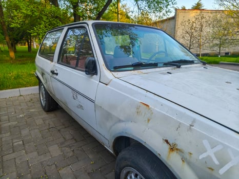 A white car with a black stripe on the side is parked on a brick road. The car is old and has a rustic appearance photo