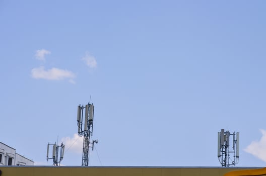 A row of cell phone towers are on top of a building. The sky is clear and blue photo