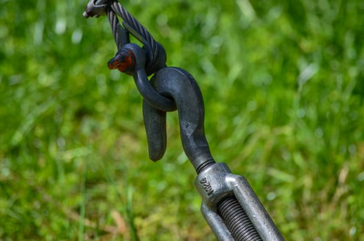 A black and silver chain is hanging from a rope. The chain is attached to a hook and is hanging from a grassy area photo