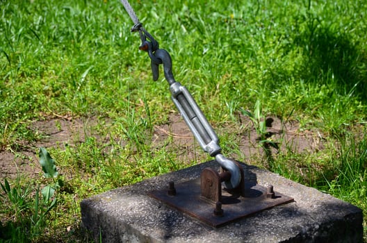 A chain is attached to a metal object on a cement slab. The chain is attached to a rope, which is tied to a tree. The scene is peaceful and serene, with the grass photo
