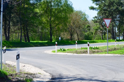 A road with a white line and a red and white sign. The road is curvy and has a lot of trees in the background photo