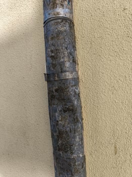 A rusty pipe is leaning against a wall. The pipe is covered in dirt and has a few holes in it photo