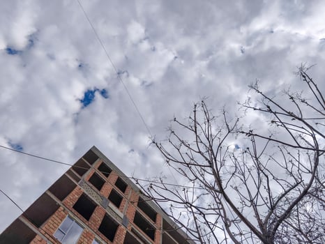 A building with a lot of empty space and a tree in front of it. The sky is cloudy and the sun is shining through the clouds photo
